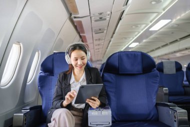 Asyalı genç bir kadın uçuşta birinci sınıfta pencere kenarında otururken, seyahat ve iş konsepti kullanıyor. Yüksek kalite fotoğraf