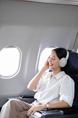 Uçakta oturan ve akıllı telefon kullanan Asyalı kadın uçak koltuğu pencere yolculuğu ve teknoloji konseptinin yanında müzik dinliyor. Yüksek kalite fotoğraf