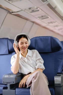Uçakta oturan ve akıllı telefon kullanan Asyalı kadın uçak koltuğu pencere yolculuğu ve teknoloji konseptinin yanında müzik dinliyor. Yüksek kalite fotoğraf