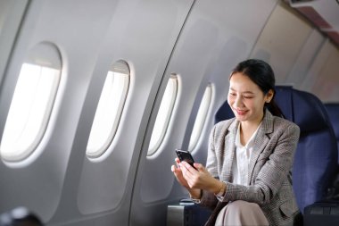 Genç Asyalı kadın uçakta oturuyor ve akıllı telefonla konuşuyor. Genç bayan gezgin cep telefonuyla konuşuyor. Yüksek kalite fotoğraf