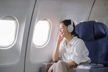Uçakta oturan ve akıllı telefon kullanan Asyalı kadın uçak koltuğu pencere yolculuğu ve teknoloji konseptinin yanında müzik dinliyor. Yüksek kalite fotoğraf
