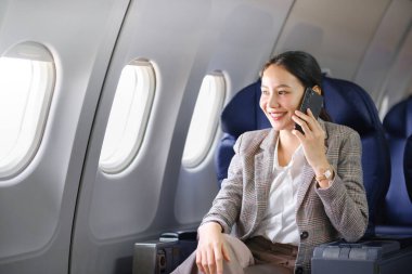 Genç Asyalı kadın uçakta oturuyor ve akıllı telefonla konuşuyor. Genç bayan gezgin cep telefonuyla konuşuyor. Yüksek kalite fotoğraf