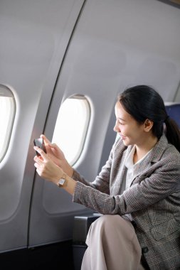 Genç Asyalı kadın uçakta oturuyor ve akıllı telefonla konuşuyor. Genç bayan gezgin cep telefonuyla konuşuyor. Yüksek kalite fotoğraf