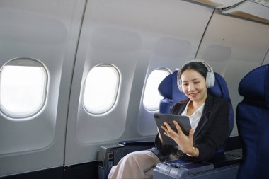 Asyalı genç bir kadın uçuşta birinci sınıfta pencere kenarında otururken, seyahat ve iş konsepti kullanıyor. Yüksek kalite fotoğraf