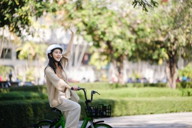 Halka açık parkta bisiklet süren ve el sallayan mutlu Asyalı kadın. Yüksek kalite fotoğraf.