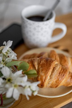 Sıcak bir sabahın tadını çıkarın. Yatağın üzerinde bir kahvaltı tepsisi, içinde taze Fransız kruvasanları, kahve ve küçük bir çiçek var..
