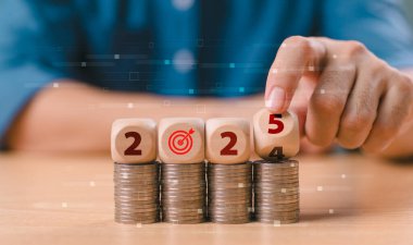 Yeni yıl 2025, bütçe planı konsepti. İşadamı 2024 'ün sonundan 2025' e kadar madeni para yığını ve kurulum vergisi hedefiyle tahta blok küpünü elle çevirmiş. Hedef ve hedef iş maliyeti. Para yönetimi