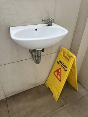 Uyarı ıslak yer sarı uyarı tahtası, umumi tuvalette mavi yer kurutma makinesiyle lavabonun altında.