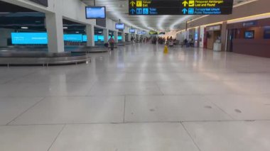 Havaalanı bagaj bölümü Gezginler ve Temiz İşaretli. İyi aydınlatılmış bir havaalanı bagaj teslim alanı modern konforları, yön işaretlerini ve uzak mesafeden birkaç yolcuyu gösteriyor..