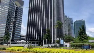 Modern Gökdelenleri ve Bulutlu Gökyüzü Göstergesi Cityscape Citarta Endonezya. Yüksek gökdelenler ve kısmen bulutlu bir gökyüzü altında modern binalarla çevrili hareketli bir şehir caddesi manzarası.