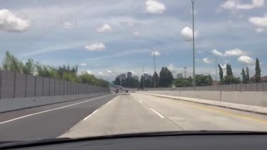 Dashcam görüntüsü Highway 'de mavi gökyüzü ve Skyline binası olan bir araba sürüyor. Parlak ve açık bir günde mavi gökyüzünün altındaki bir şehir manzarasına giden sessiz bir otoyol bulunur..