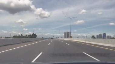 Dashcam görüntüsü Highway 'de mavi gökyüzü ve Skyline binası olan bir araba sürüyor. Parlak ve açık bir günde mavi gökyüzünün altındaki bir şehir manzarasına giden sessiz bir otoyol bulunur..