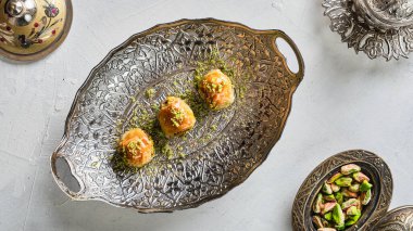 Beyaz bir zeminde, gümüş ve bakır çatal bıçaklarla çevrili beyaz bir tabakta fıstıklı doğu tatlıları.