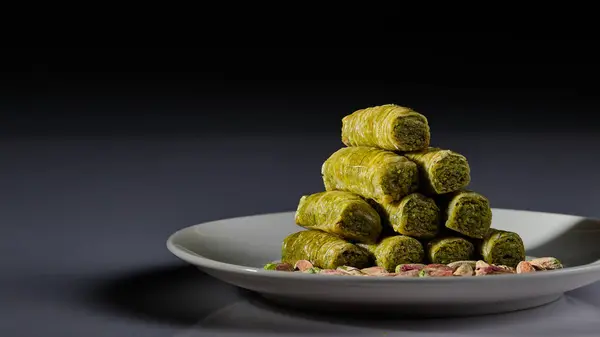 Beyaz arka planda ve gri ve siyah arkaplanda fıstıklı bir tabak Arap tatlısı.