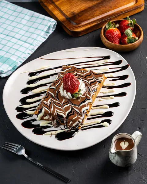 Siyah arka planda çikolata ve çilekli bir tabak waffle.