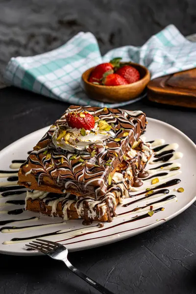 Siyah arka planda çikolata ve çilekli bir tabak waffle.