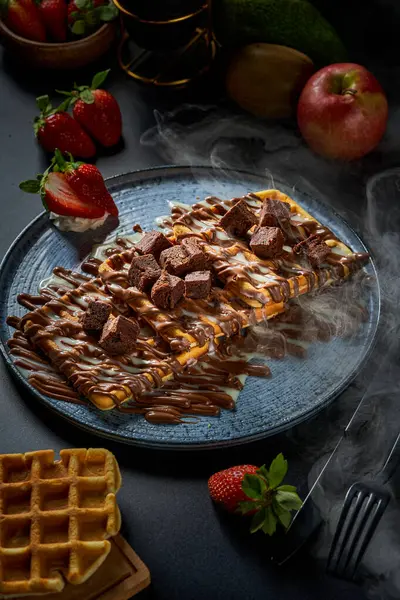 A plate of waffles with chocolate on a black background
