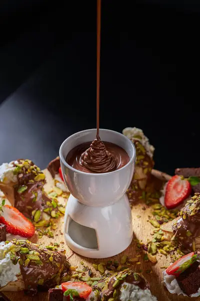 Muz, çilek ve şam fıstığı parçalarıyla ahşap bir zeminde bir fincan sıcak çikolatanın içine yakın plan çikolata döküldü..
