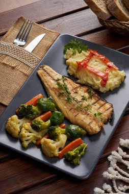 Ahşap zeminde kaynamış sebzeli bir tabak uskumru.