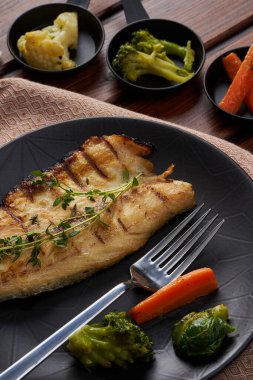 Ahşap zeminde kaynamış sebzeli bir tabak uskumru.