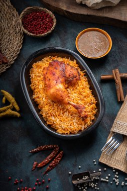 Koyu yeşil arka planda ızgara tavuk eti ve baharatlı Mandi pilavı.