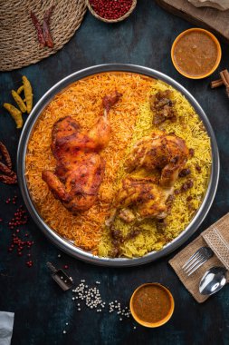 Koyu yeşil arka planda ızgara tavuk eti ve baharatlı Mandi pilavı.