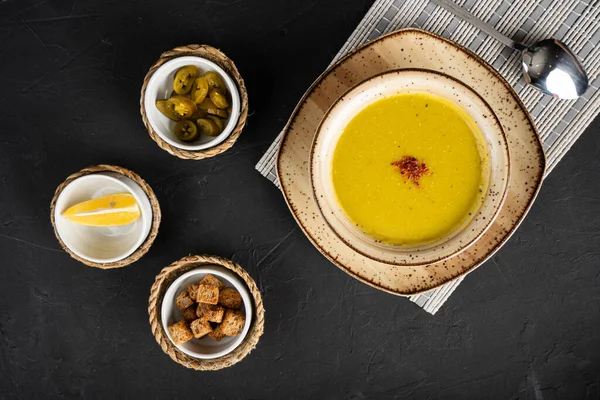 Bir tabak mercimek çorbasının üstünde siyah ahşap bir zeminde kızarmış ekmek.