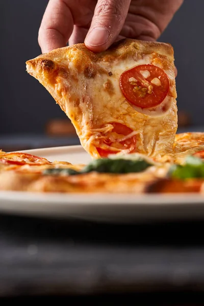 一个年轻人的手拿着一块装有奶酪和西红柿的披萨 — 图库照片