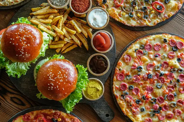 A picture of several dishes of pizza, burgers, french fries, and sauces