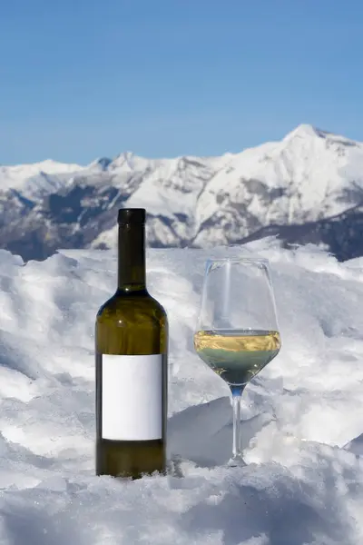 a bottle of wine and a glass of wine on a snowy mountain