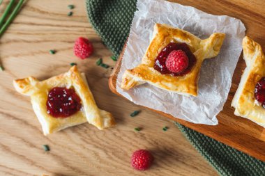 Camembert peyniri ve ahududu reçeli ile doldurulmuş lezzetli puf börekleri, ahşap bir tahtada taze ahududu ile servis edilir. Tasarım ve baskı için üst görünüm yiyecek fotoğrafçılığı.