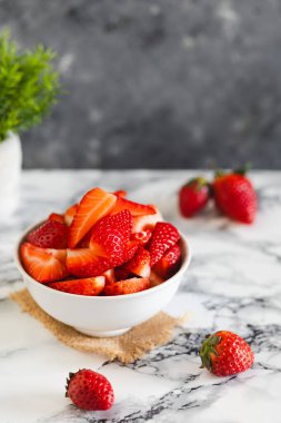 Canlı, taze dilimlenmiş çilekler mermer bir yüzey üzerinde beyaz bir kasede servis edilir, tatlı ya da atıştırmak için mükemmeldir..