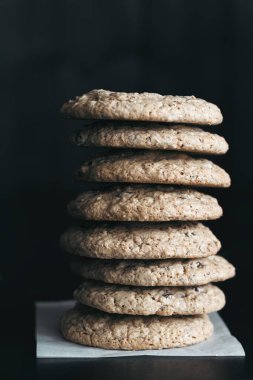 Uzun bir yığın ev yapımı glütensiz çikolata parçacıklı kurabiyeler kırsal dokuya sahip, parşömen kağıdının üzerine koyulmuş koyu bir arka plan.