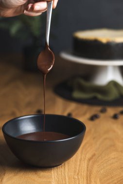 Elinde bir kaşık, yumuşak, erimiş çikolatayı siyah bir klozete damlatıyor ve arkasında da peynirli kek duruyor..