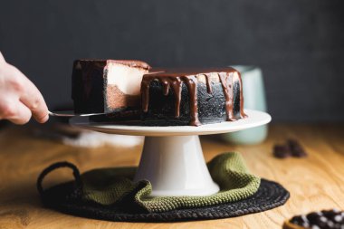 Koyu kabuklu zengin bir peynirli keki dilimlemek, kremalı vanilya ve çikolata katmanlı, üzeri parlak çikolata ganache ile kaplı.