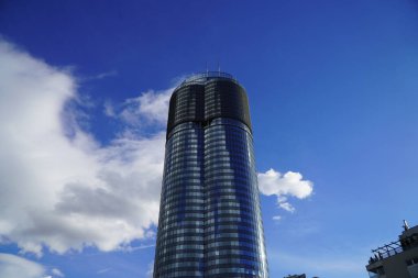 Mavi camlı, güneşli gökyüzünü yansıtan tek bir modern ofis binası.