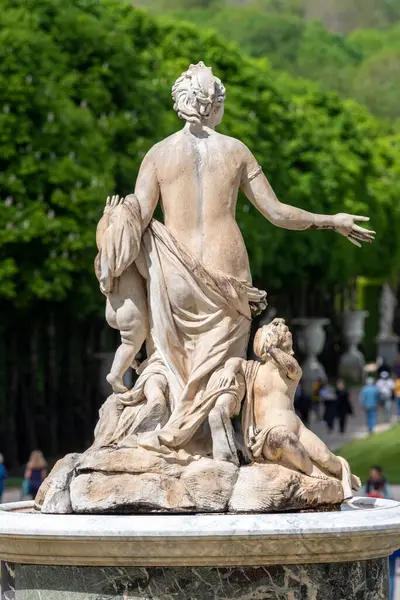 back of a woman statue, with kids in the fountain outside the palace of Versailles with people walking in the distance