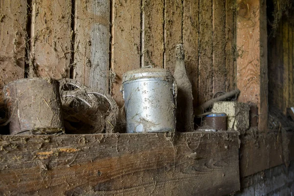 Örümcek ağları ve tozlu klasik metal süt sürahisi, eski bir ahırda saklanmış, şişeler ve çiftlik eşyalarıyla.