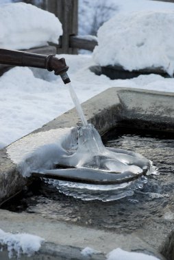 Eski çağlardan kalma bir çeşme soğuk su akıtıyor ve beton bir gölette buz kulesi oluşturuyor.