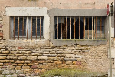 Kırık camları ve paslı metal parmaklıkları olan eski, terk edilmiş bir evin taşlı duvarı.