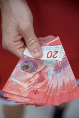 A hand holding a fanned-out stack of Swiss 20 franc banknotes, symbolising money, finance, and wealth