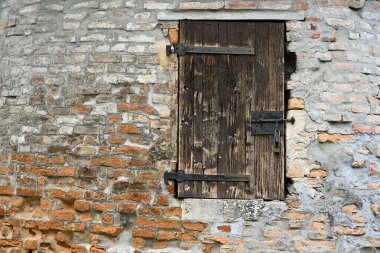 Fransa 'da tarihi mimari ve ortaçağ çekiciliğini yansıtan antik bir kulenin taş duvarında demirden menteşeleri olan taşralı tahta bir kapı.