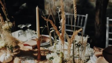 Yakın çekimde düğün masası dışarıda servis edilir ve sonbahar toprak renkleri ile süslenir. Doğal sonbahar bohem çiçekleri düğün yemeği, tabaklar ve şarap bardakları için..