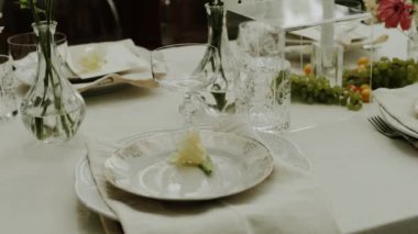 Serada sunulan ve pastel çiçeklerle dekore edilen düğün masasının yakın plan resmi. Minimalist doğal düğün yemeği, tabaklar ve şarap bardakları için. Çekim yapan kimse yok, yavaş çekim. Yüksek kalite