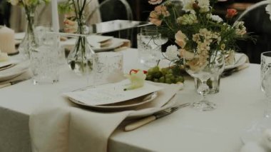 Serada sunulan ve pastel çiçeklerle dekore edilen düğün masasının yakın plan resmi. Minimalist doğal düğün yemeği, tabaklar ve şarap bardakları için. Çekim yapan kimse yok, yavaş çekim. Yüksek kalite