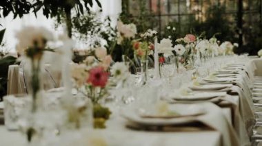 Doğal düğün yemeği, tabaklar ve şarap kadehleri için pastel çiçeklerle servis edilen orta boy düğün masası. Çekim yapan kimse yok, yavaş çekim. Yüksek kalite