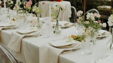 Serada sunulan ve pastel çiçeklerle dekore edilen düğün masasının yakın plan resmi. Minimalist doğal düğün yemeği, tabaklar ve şarap bardakları için. Çekim yapan kimse yok, yavaş çekim. Yüksek kalite