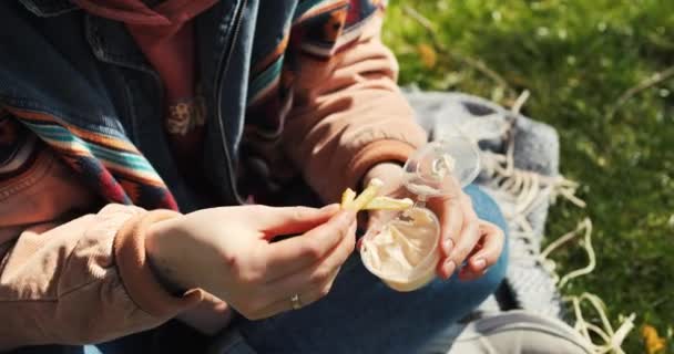 若い大人の女性は 公園でフランスのフライドポテトを取り出します 食べ物と春の日差しを楽しんでいる 高品質の4K映像 — ストック動画