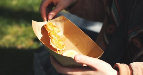 美丽的年轻女子在公园里吃街头食物 享受春天的阳光 女孩吃烤虾仁 高质量的4K镜头 — 图库视频影像