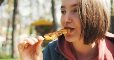 Güzel genç bir kadın parkta sokak yemeği yiyor, bahar güneşinin tadını çıkarıyor. Kız ızgara karides yiyor. Yüksek kalite 4k görüntü
